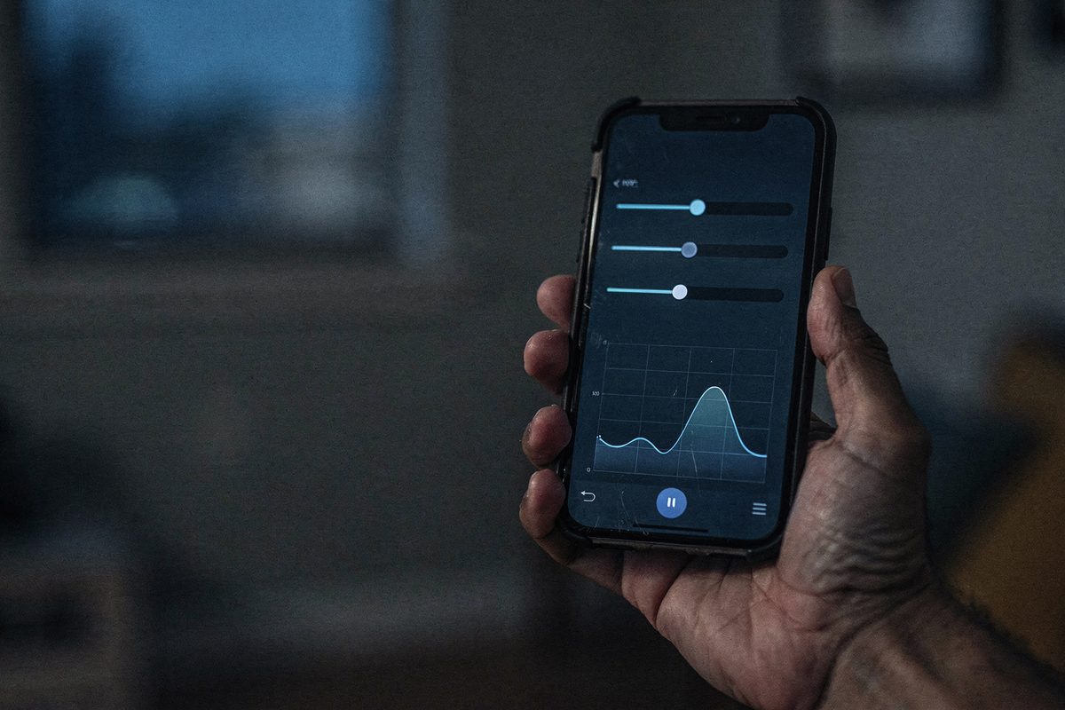A hand holding a phone with a voice-changer mobile app open, showing sliders and a waveform